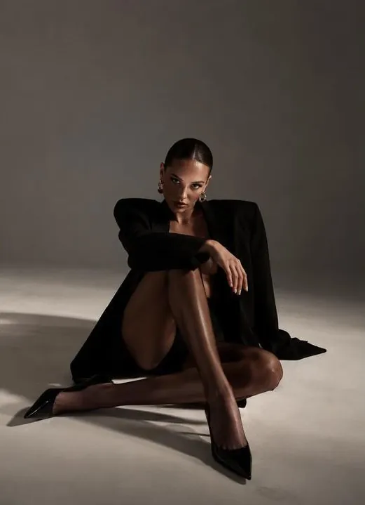 Modelo sentada em fundo cinza com blazer preto